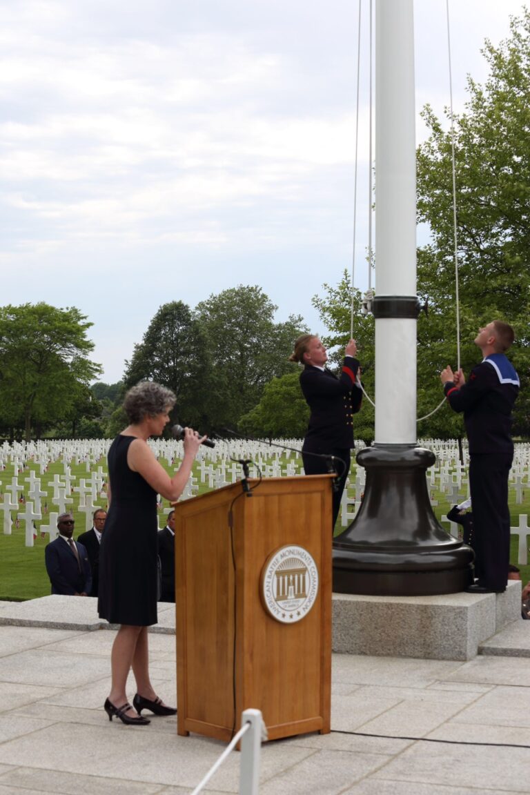 A women sings the National Anthem as the flag is raised during the 2017 Memorial Day Ceremony at Brittany American Cemetery.