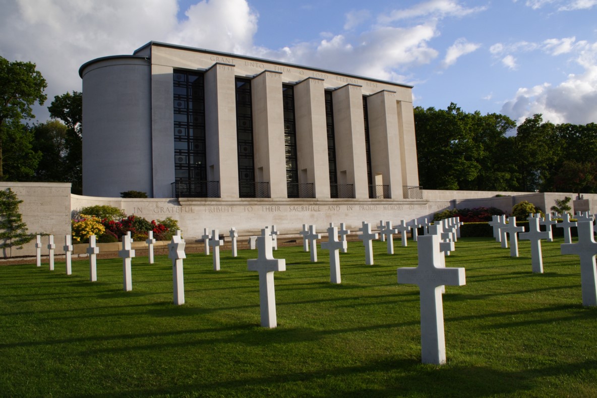 View of Cambridge American Cemetery with rows of white crosses and the chapel, set against a backdrop of green lawns and trees