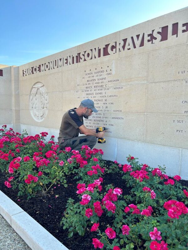 A man drills a hole in a stone wall at Epinal American Cemetery 