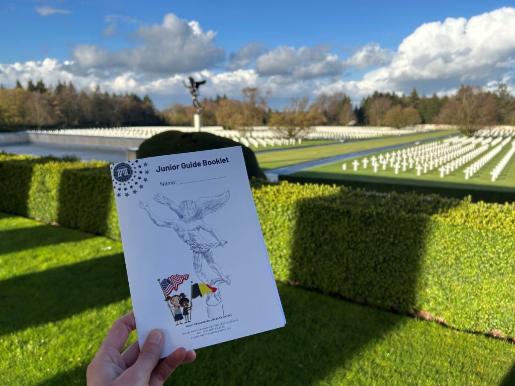 A guide at Henri-Chapelle American Cemetery in Belgium holds the Junior Guide booklet for their site. Each site-specific booklet includes activities tailored specifically for children to engage them in learning about ABMC and the stories of those commemorated there. (ABMC photo).