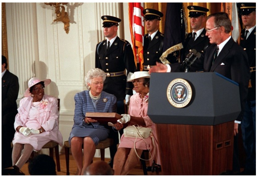 Medal of Honor presentation to Cpl. Freddie Stowers’ sisters at the White House, April 24, 1991, Stowers, a native of Anderson County, South Carolina, received the medal for action during World War I. President George H. W. Bush, Mrs. Barbara Bush, and Mary Bowens admire the Medal of Honor certificate. Bowens is Stowers' sister. His other sister Georgina Palmer (far left) looks on. Stowers was the first African American to receive the Medal of Honor for action during World War I. Credit: Robert Ward, DOD PA, Photo DD-SC-02-05877 at defenseimagery.mil (public domain).